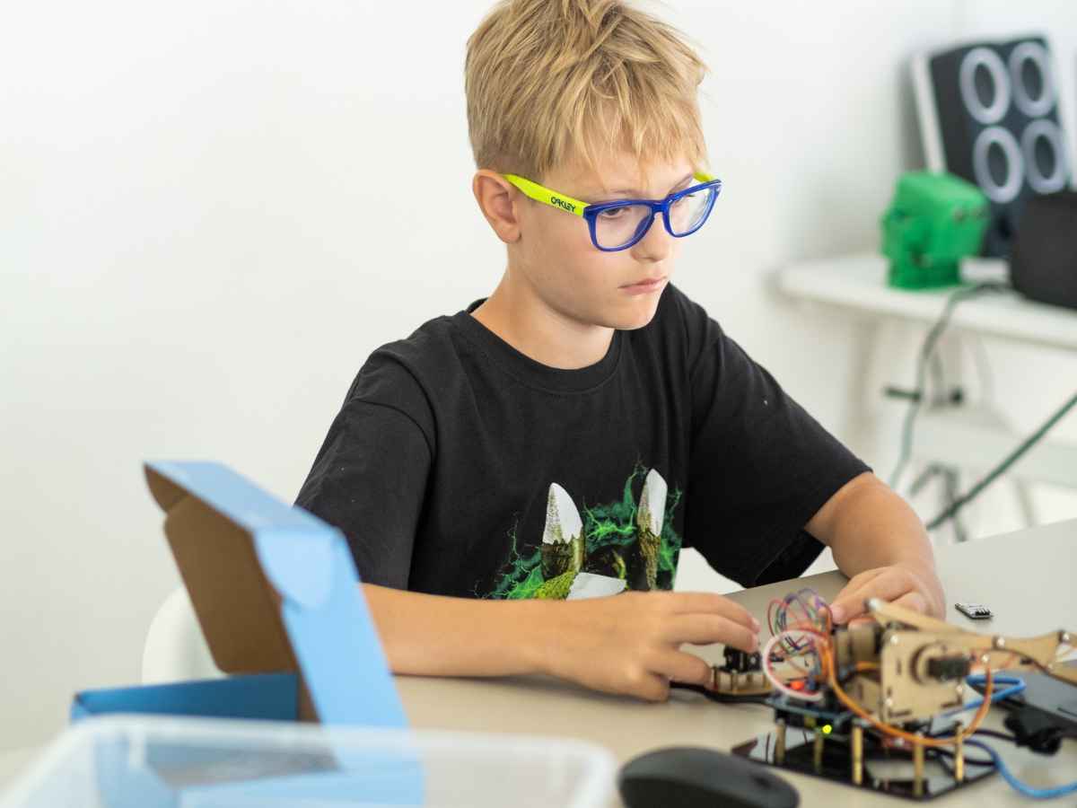 Junge arbeitet konzentriert an einem selbstgebauten Roboterarm-Manipulator aus Holz und Elektronik.