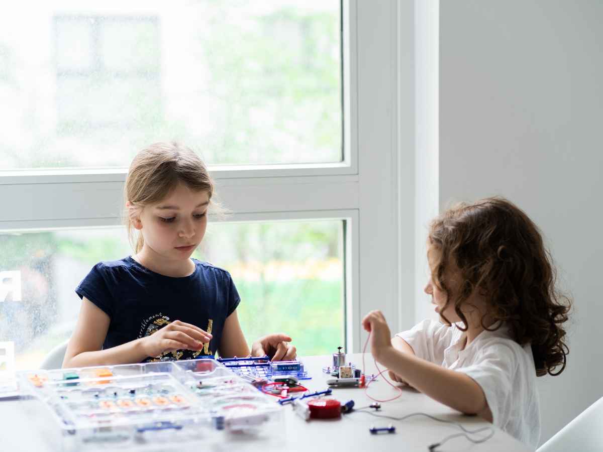 Zwei Kinder bauen einfache elektronische Schaltkreise mit Steckbauteilen am Tisch.