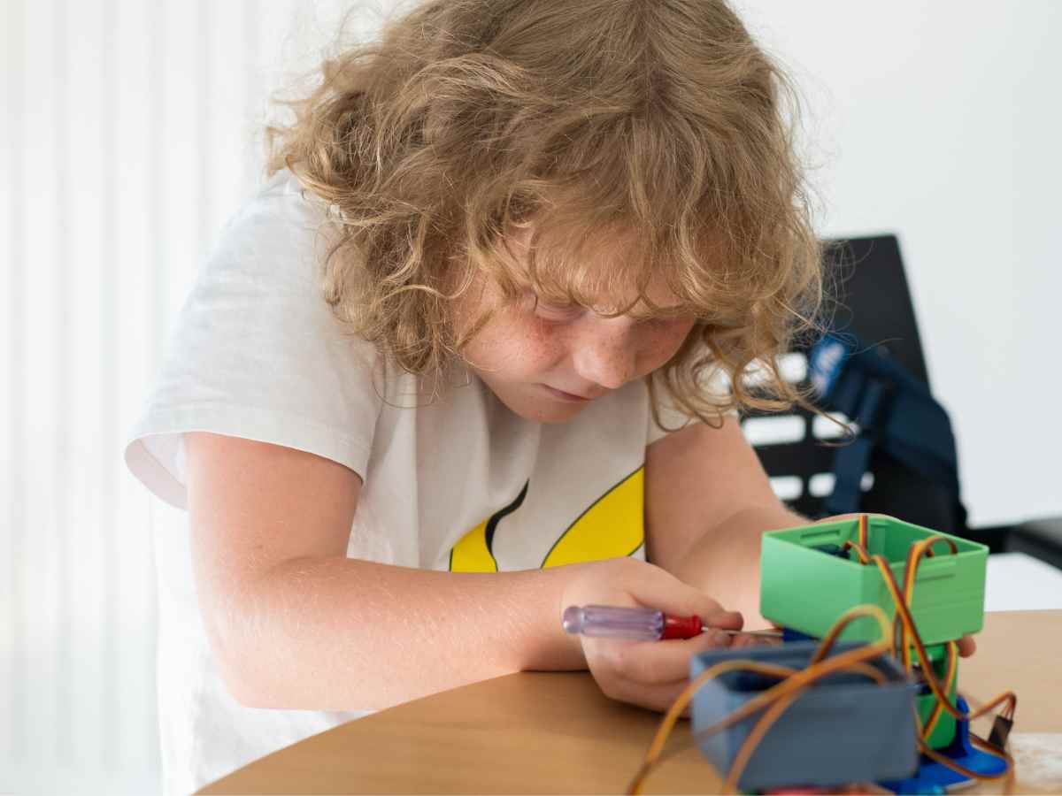 Kind baut den zweibeinigen Lernroboter Otto mit Schraubendreher und elektronischen Bauteilen zusammen.
