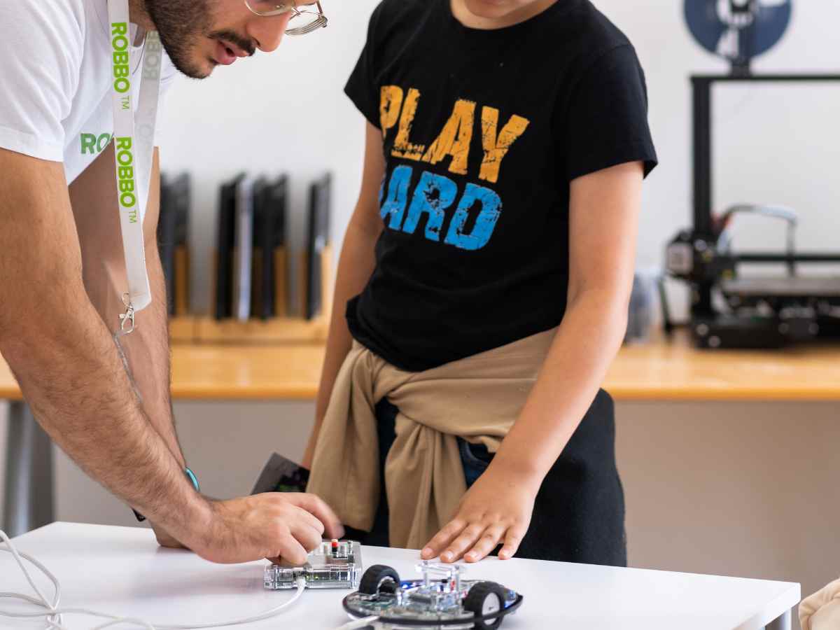 Kind und Trainer arbeiten gemeinsam an einem kleinen Roboter