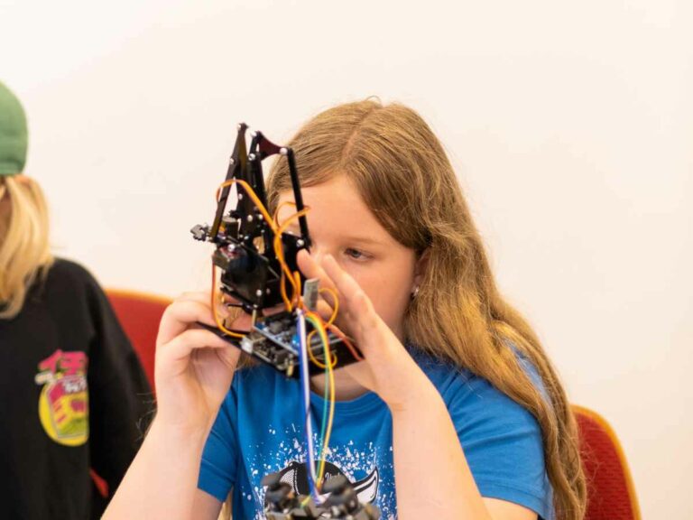 Mädchen arbeitet konzentriert an einem komplexen Roboter mit Kabeln und mechanischen Bauteilen.