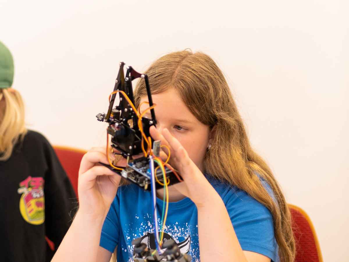 Mädchen arbeitet konzentriert an einem komplexen Roboter mit Kabeln und mechanischen Bauteilen.