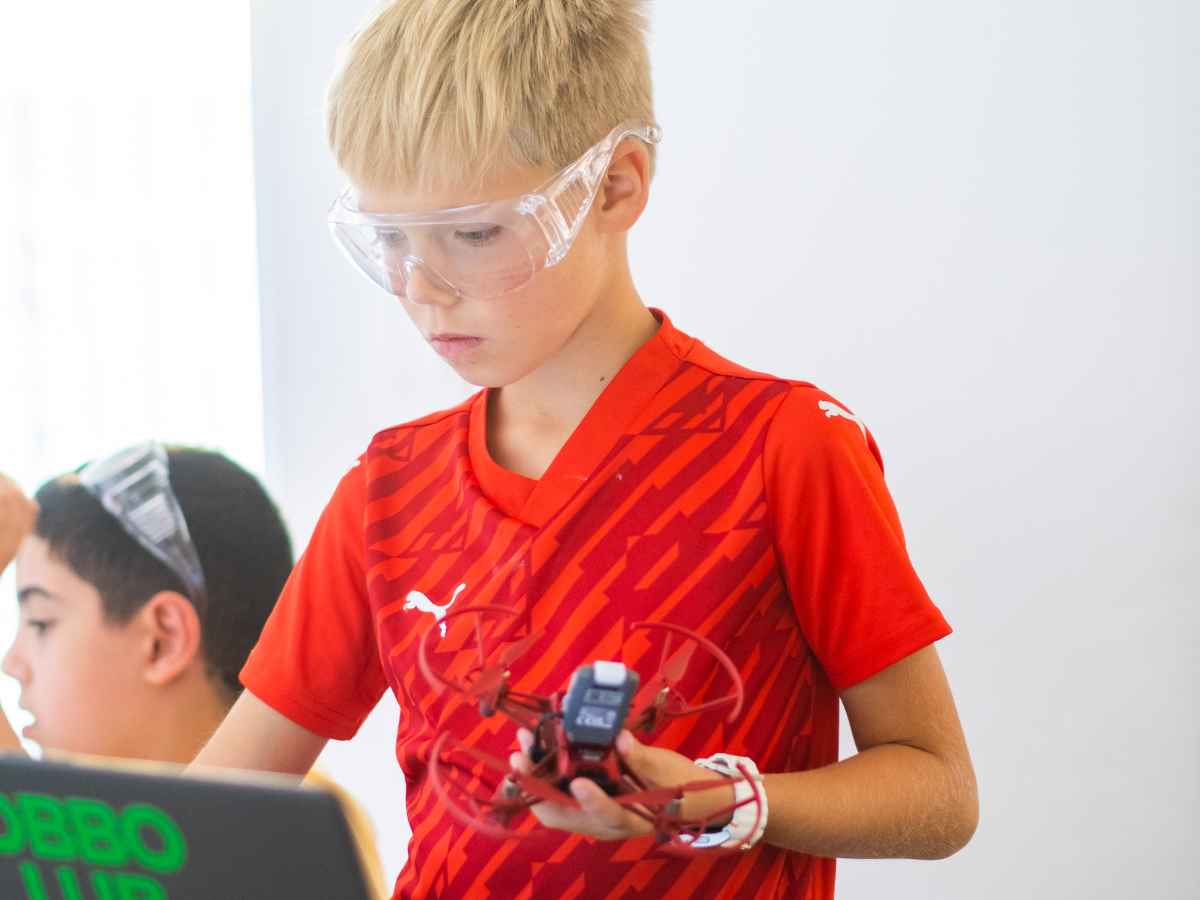 Junge mit Schutzbrille hält eine kleine Trainingsdrohne während eines Robotikunterrichts.