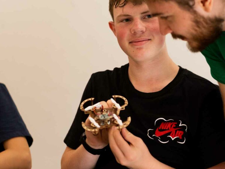 Jugendlicher hält einen kleinen selbstgebauten Trainingsdrohnen-Prototyp und spricht mit einem Trainer.