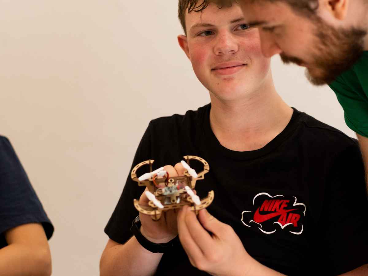 Jugendlicher hält einen kleinen selbstgebauten Trainingsdrohnen-Prototyp und spricht mit einem Trainer.