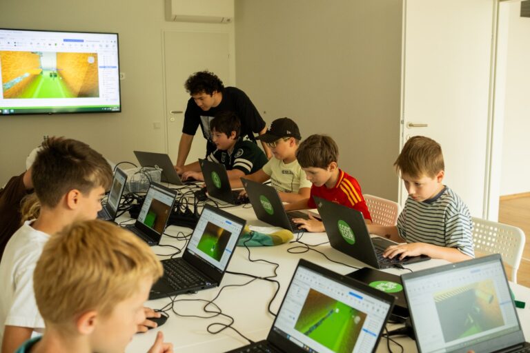 Kinder programmieren an Laptops im ROBBO Club 1030, ein Trainer hilft an einem Bildschirm